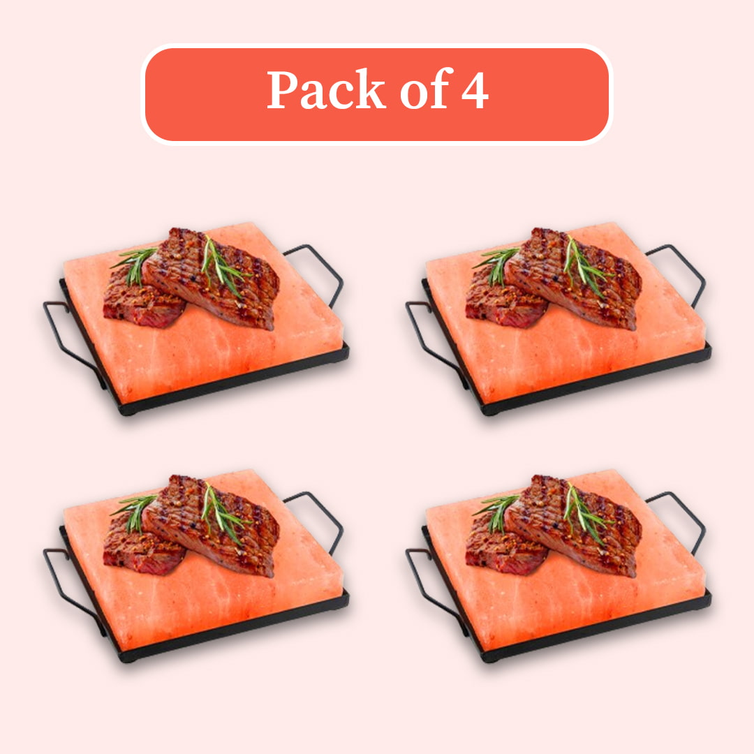Four identical rectangular salt stone grills with black metal handles, each topped with grilled steak and rosemary, arranged in a 2x2 grid on a pale pink background with an orange label reading 'Pack of 4'.