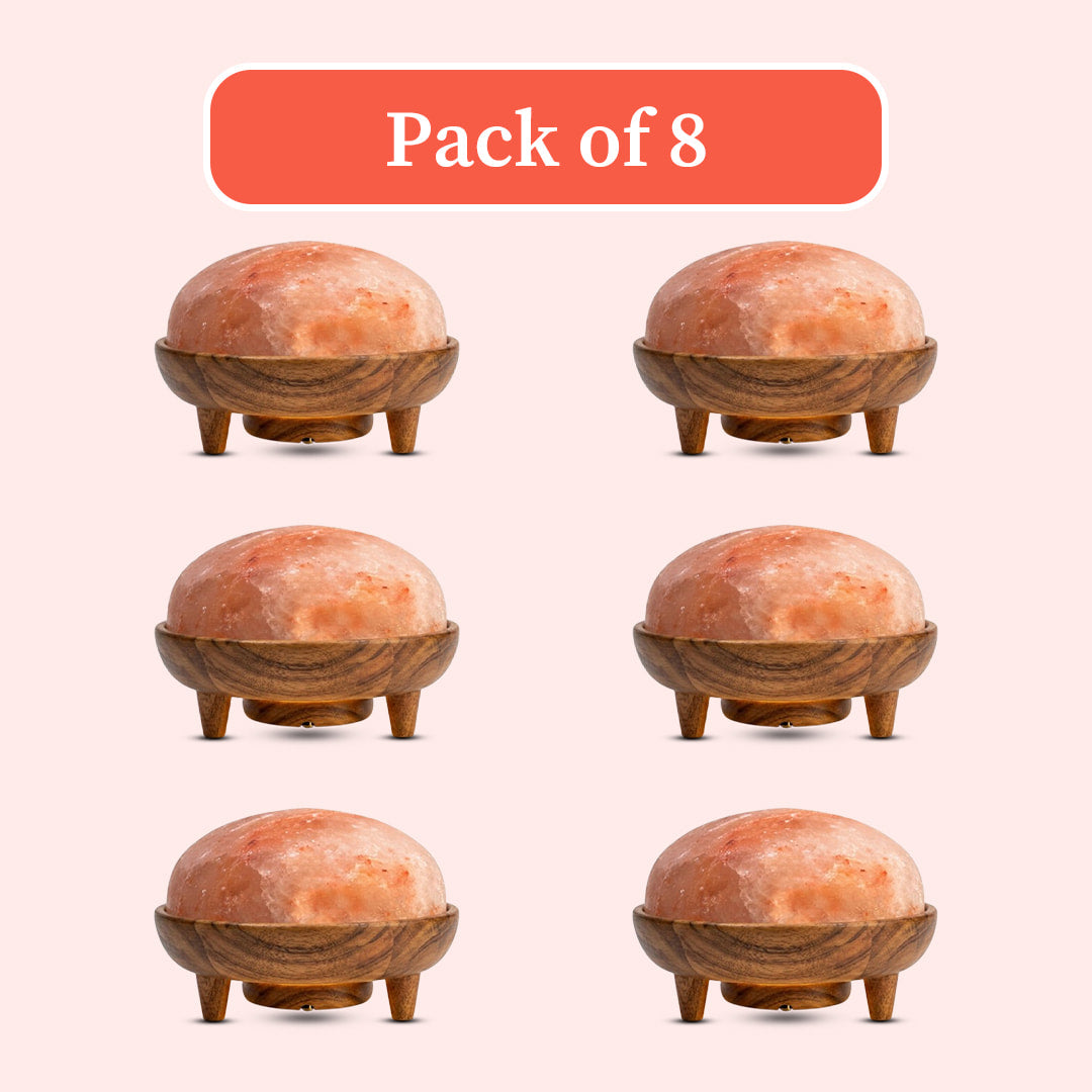 Six views of a dome-shaped pink salt lamp in a carved wooden base with three legs, arranged in a grid under a coral label that reads 'Pack of 8' on a pale pink background.